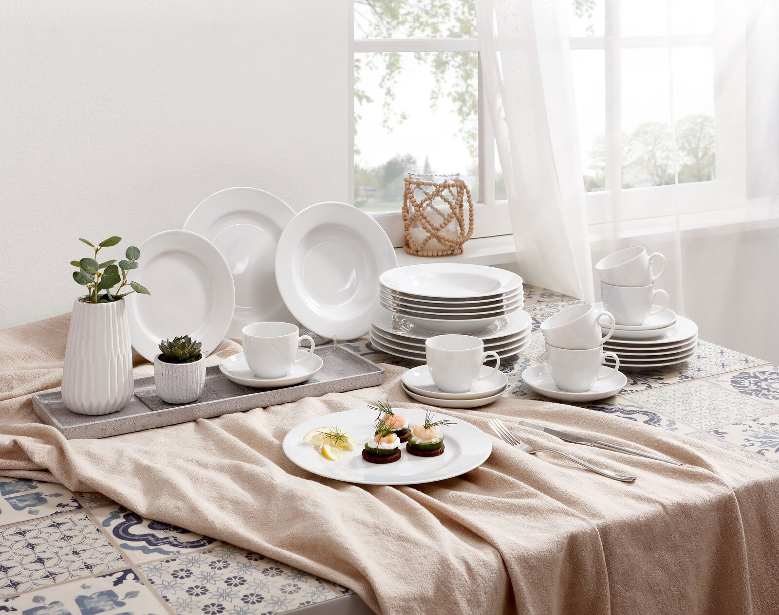 Seltmann Weiden Kombiservice 30-tlg. RONDO Ein stilvolles Kombiservice Rondo Weiß 30-tlg, präsentiert auf einem Tisch mit dekorativen Elementen und natürlichem Licht von einem Fenster im Hintergrund. Die Perspektive zeigt das Service von schräg oben.