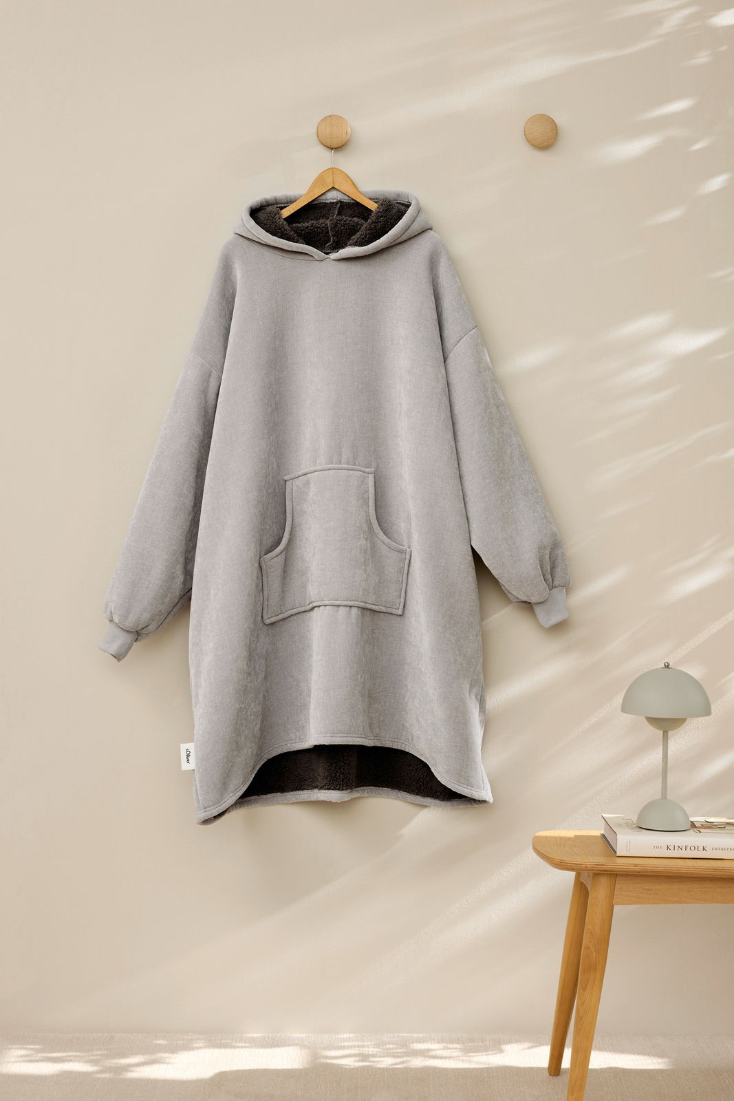 Grauer Lounge Hoodie mit Kapuze und Kängurutasche, frontal an einem Haken hängend, mit weichem Innenfutter.