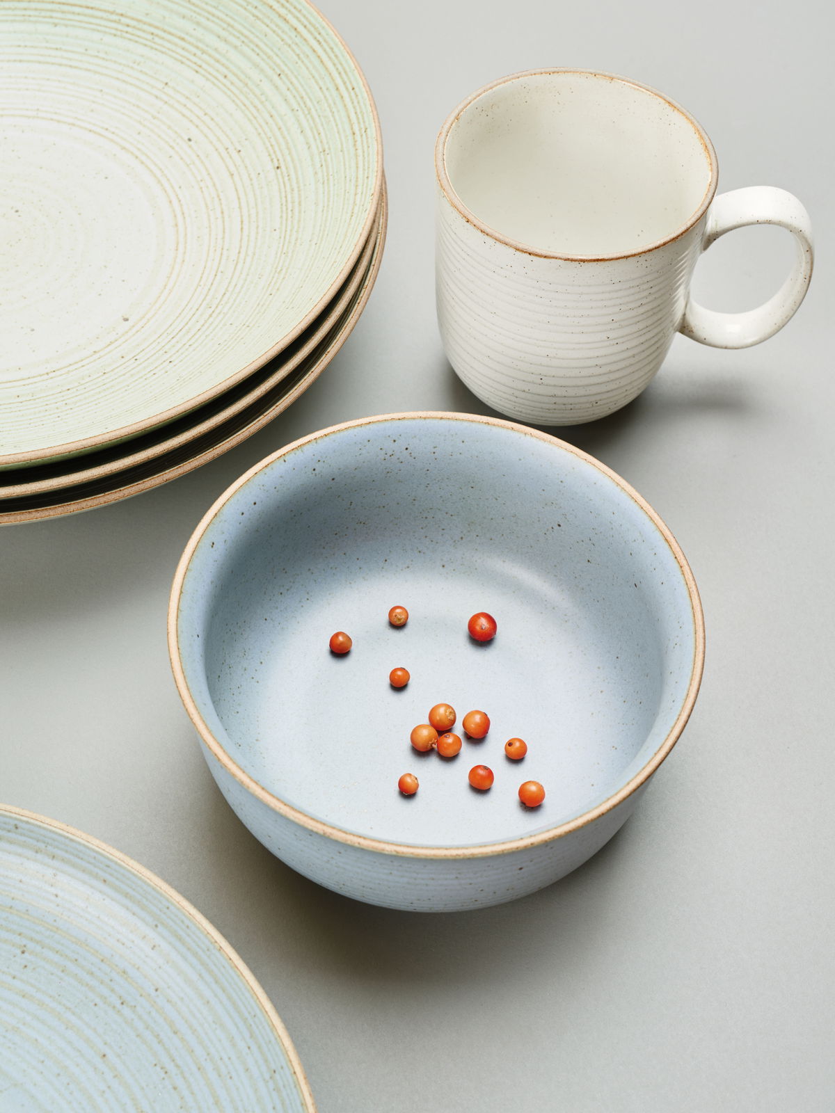 Thomas Kaffeebecher NATURE Keramikbecher mit Henkel in cremeweißer Farbe, umgeben von Tellern und einer Schale, aus der Vogelperspektive fotografiert.