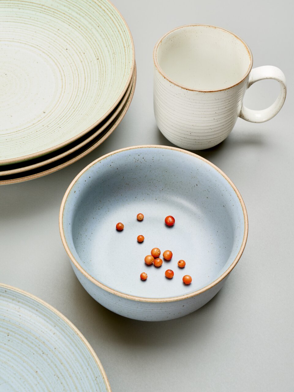 Thomas Kaffeebecher NATURE Keramikbecher mit Henkel in cremeweißer Farbe, umgeben von Tellern und einer Schale, aus der Vogelperspektive fotografiert.