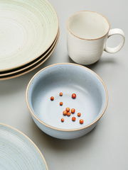 Keramikbecher mit Henkel in cremeweißer Farbe, umgeben von Tellern und einer Schale, aus der Vogelperspektive fotografiert.