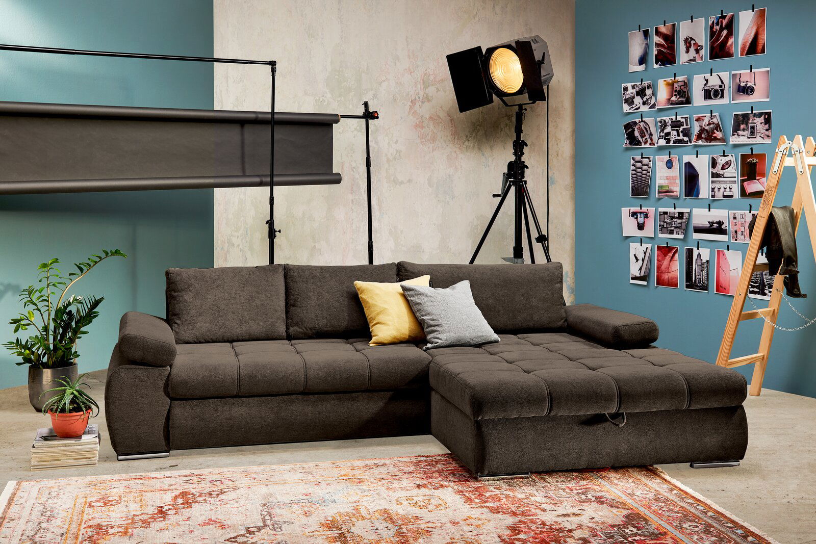 Braune Rundecke mit Ottomane rechts, dekoriert mit gelben und grauen Kissen, in einem stilvollen Raum mit Fotowand und Pflanzen, Perspektive von vorne.