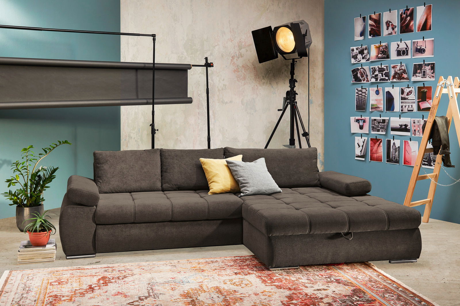 Braune Rundecke mit Ottomane rechts, dekoriert mit gelben und grauen Kissen, in einem stilvollen Raum mit Fotowand und Pflanzen, Perspektive von vorne.