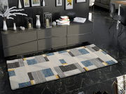 Moderner Teppich mit geometrischem Muster in Blau, Grau und Gelb auf dunklem Marmorboden, perspektivisch von oben betrachtet.