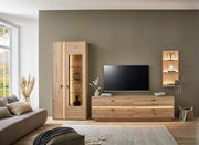 Moderne Wandkombination aus Holz in einem Wohnzimmer, bestehend aus einem hohen Schrank mit Glaselementen, einem TV-Board und einem Wandregal, seitliche Perspektive.