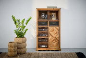 Houten ladekast met verschillende lades en deurtjes, versierd met opdrukken en patronen, gefotografeerd vanaf de voorkant. Ernaast staat een plant in een gevlochten mand.