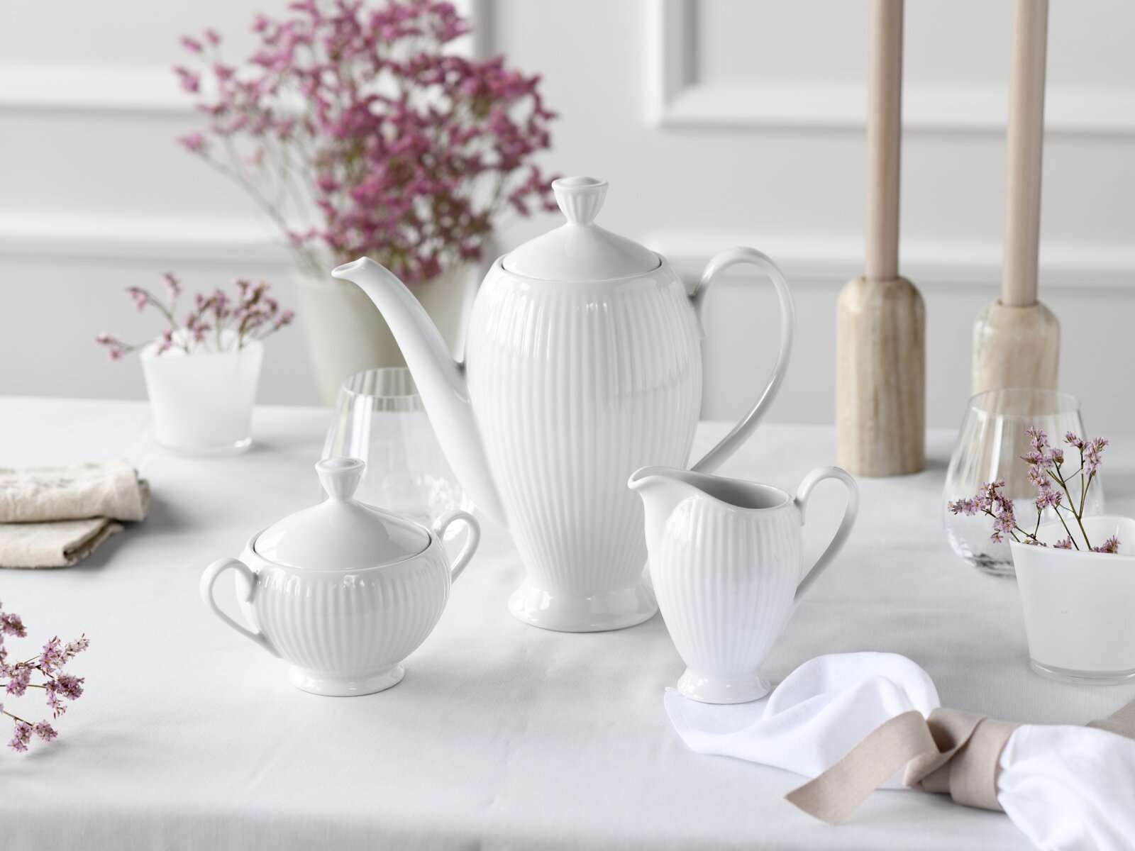 Weißes geriffeltes Porzellan-Kaffeeservice mit Kaffeekanne, Zuckerdose und Milchkännchen auf gedecktem Tisch, frontal in leichter Seitenansicht fotografiert