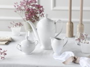 Weißes geriffeltes Porzellan-Kaffeeservice mit Kaffeekanne, Zuckerdose und Milchkännchen auf gedecktem Tisch, frontal in leichter Seitenansicht fotografiert