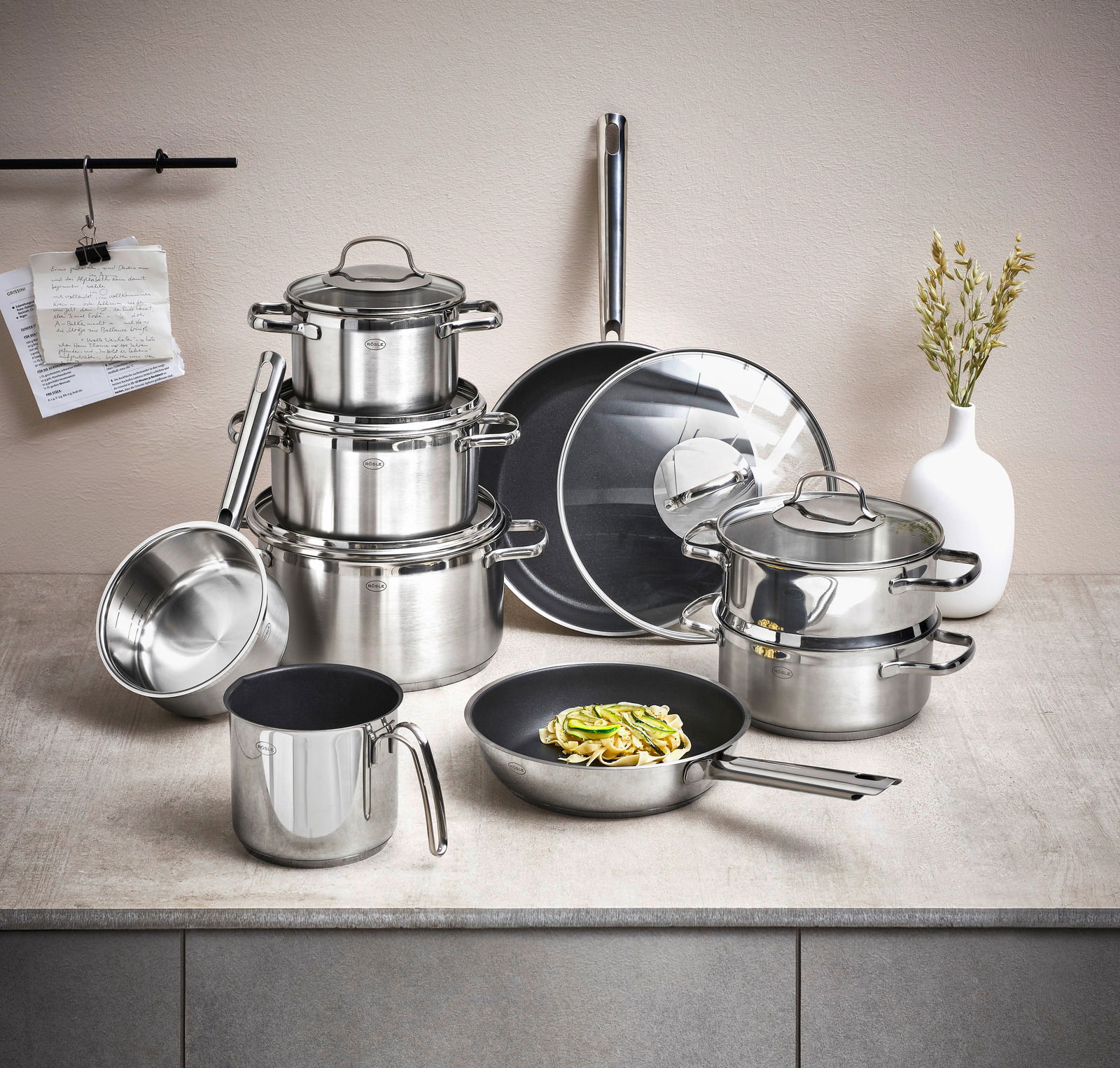 Topfset Elegance 10-tlg. aus Edelstahl, bestehend aus mehreren Töpfen und Pfannen mit Glasdeckeln, auf einer Küchenarbeitsplatte von vorne fotografiert.