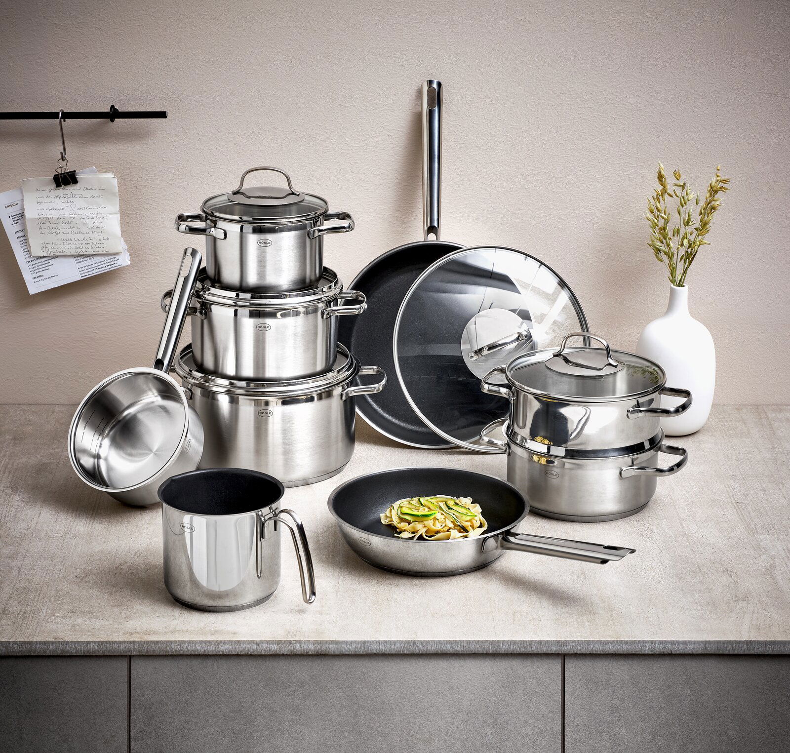 Topfset Elegance 10-tlg. aus Edelstahl, bestehend aus mehreren Töpfen und Pfannen mit Glasdeckeln, auf einer Küchenarbeitsplatte von vorne fotografiert.