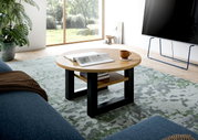 Runder Couchtisch aus Holz mit schwarzem Metallgestell, von schräg oben fotografiert, auf einem gemusterten Teppich in einem modernen Wohnzimmer.