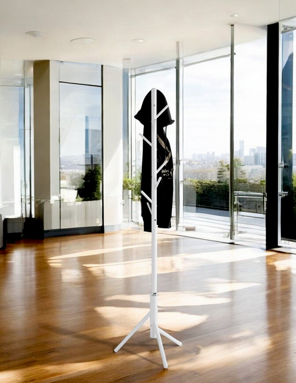 Weißer freistehender Kleiderständer/Garderobenständer mit mehreren Haken und dreibeinigem Standfuß, daran ein schwarzes Kleidungsstück, im hellen Raum mit großen Glasfronten; Perspektive: frontale Ansicht auf Augenhöhe.