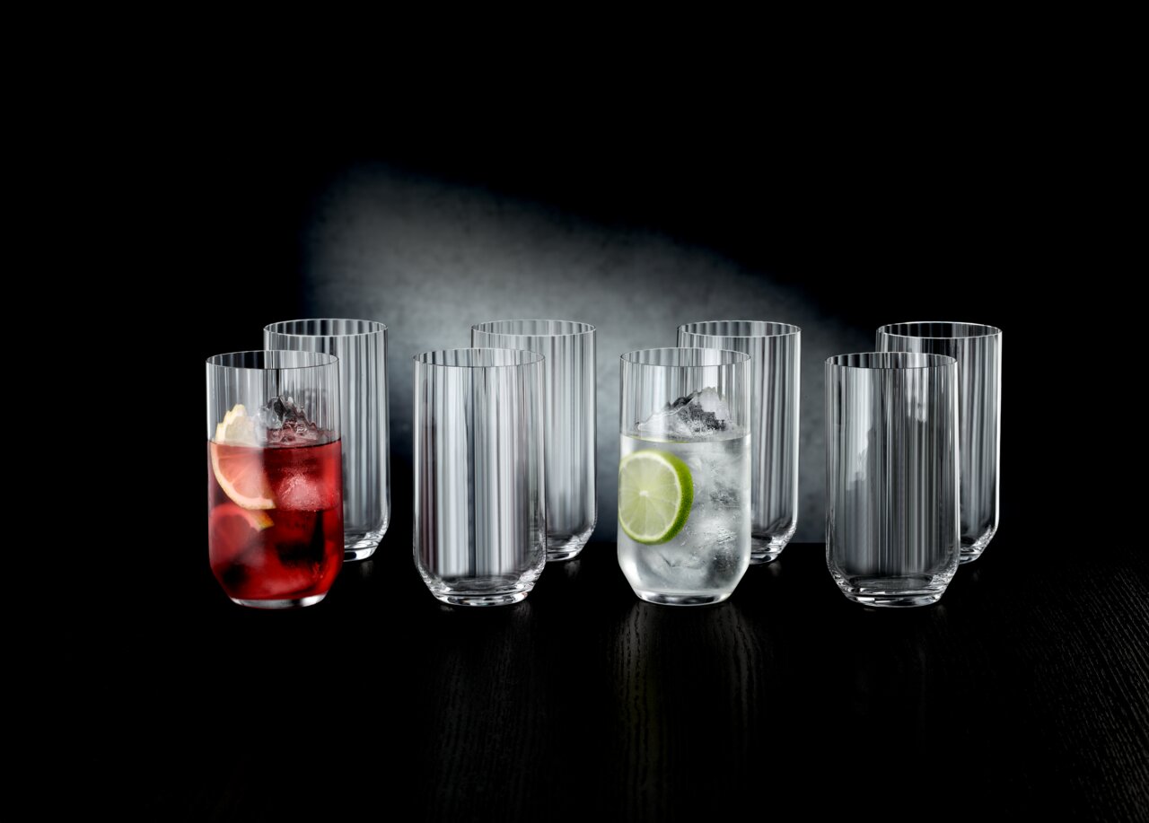 Ein Set aus acht Longdrinkgläsern, teilweise gefüllt mit Getränken und Eis, auf einem dunklen Tisch vor einem dunklen Hintergrund. Die Perspektive ist frontal.