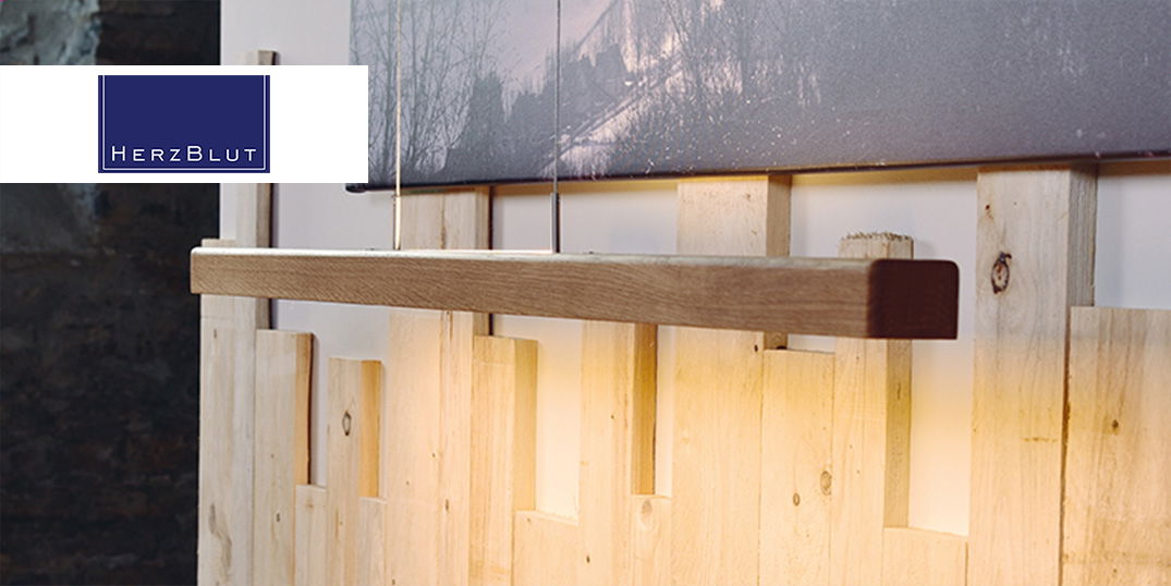 Lampe mit Holzoptik vor einer strukturierten Wand, mit dem einem dunklen Bild darüber.