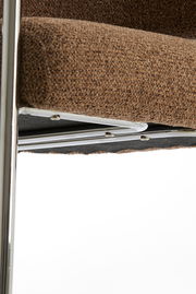 Nahaufnahme eines braunen Armlehnstuhls mit Metallrahmen, seitliche Perspektive