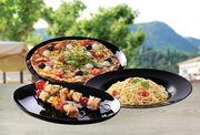Drei schwarze, glänzende Servierplatten mit Pizza, Spaghetti und Spießen auf einem Holztisch im Freien; Perspektive: leicht erhöhte Frontansicht (schräg von vorn).