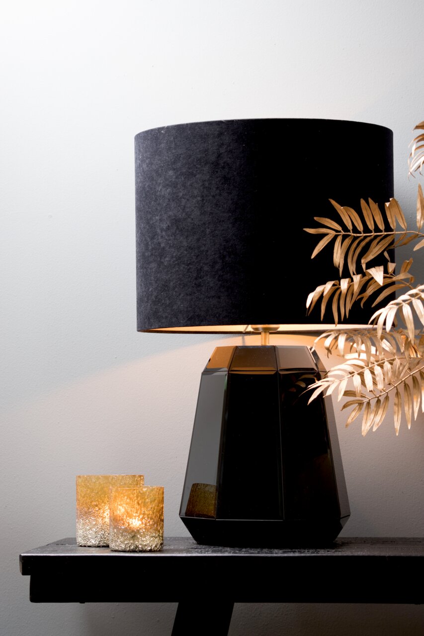 Schwarzer zylindrischer Lampenschirm auf facettiertem schwarzen Lampenfuß, seitliche Perspektive, dekoriert mit goldenen Blättern und zwei kleinen Kerzen.