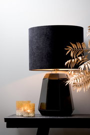 Schwarzer zylindrischer Lampenschirm auf facettiertem schwarzen Lampenfuß, seitliche Perspektive, dekoriert mit goldenen Blättern und zwei kleinen Kerzen.