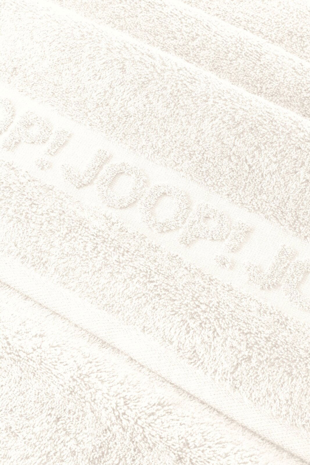 Nahaufnahme in schräger Draufsicht auf ein weißes, flauschiges Handtuch mit eingewebtem/erhabenem Schriftzug „JOOP!“.