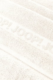 Nahaufnahme in schräger Draufsicht auf ein weißes, flauschiges Handtuch mit eingewebtem/erhabenem Schriftzug „JOOP!“.