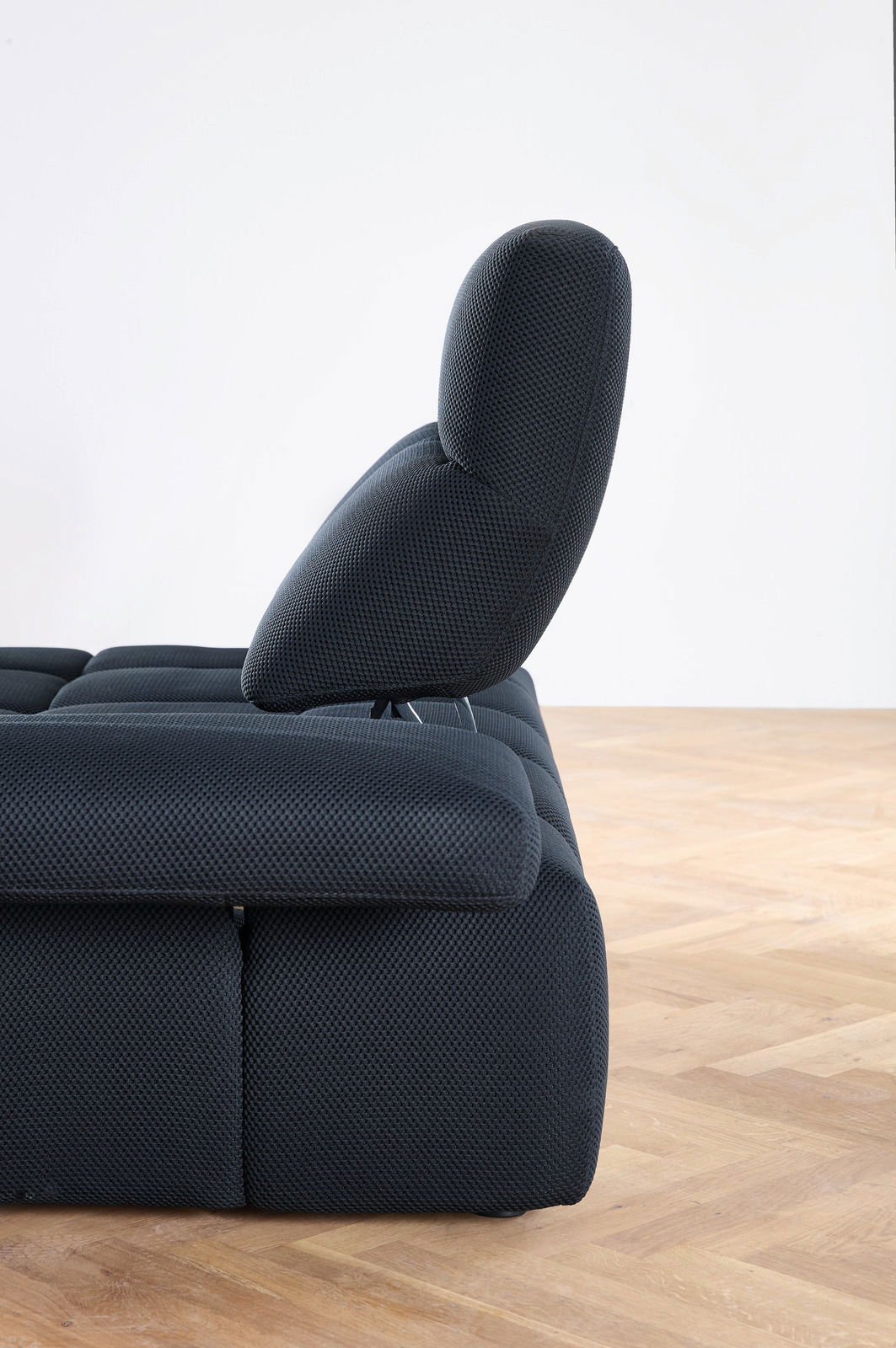 Seitenansicht einer modernen, dunkel gepolsterten Eckgarnitur mit verstellbarer Rückenlehne auf Holzfußboden.