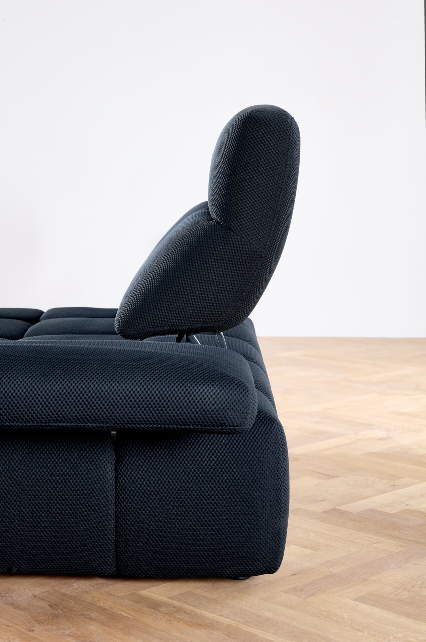 Zijaanzicht van een moderne, donker gestoffeerde hoekbank met verstelbare rugleuning op een houten vloer.