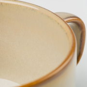 Detailaufnahme in schräger Seitenansicht von zwei stapelbaren Keramikschalen in Creme mit braunem Rand und dezenter Reaktivglasur.