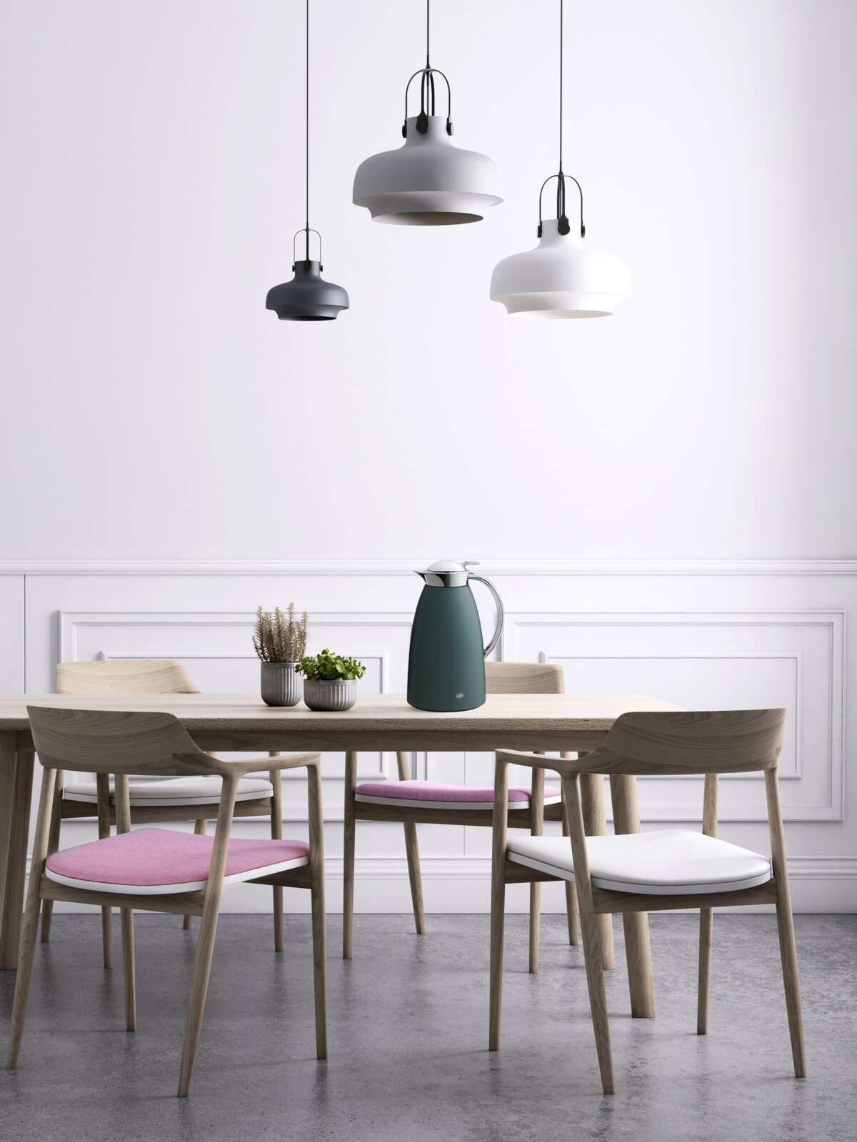 Skandinavischer Esstisch aus hellem Holz mit vier Stühlen und Sitzkissen in Rosa und Weiß, dekoriert mit Pflanzen und einer Thermoskanne darüber drei moderne Pendelleuchten in Schwarz, Grau und Weiß, frontal aus leicht erhöhter Perspektive aufgenommen.
