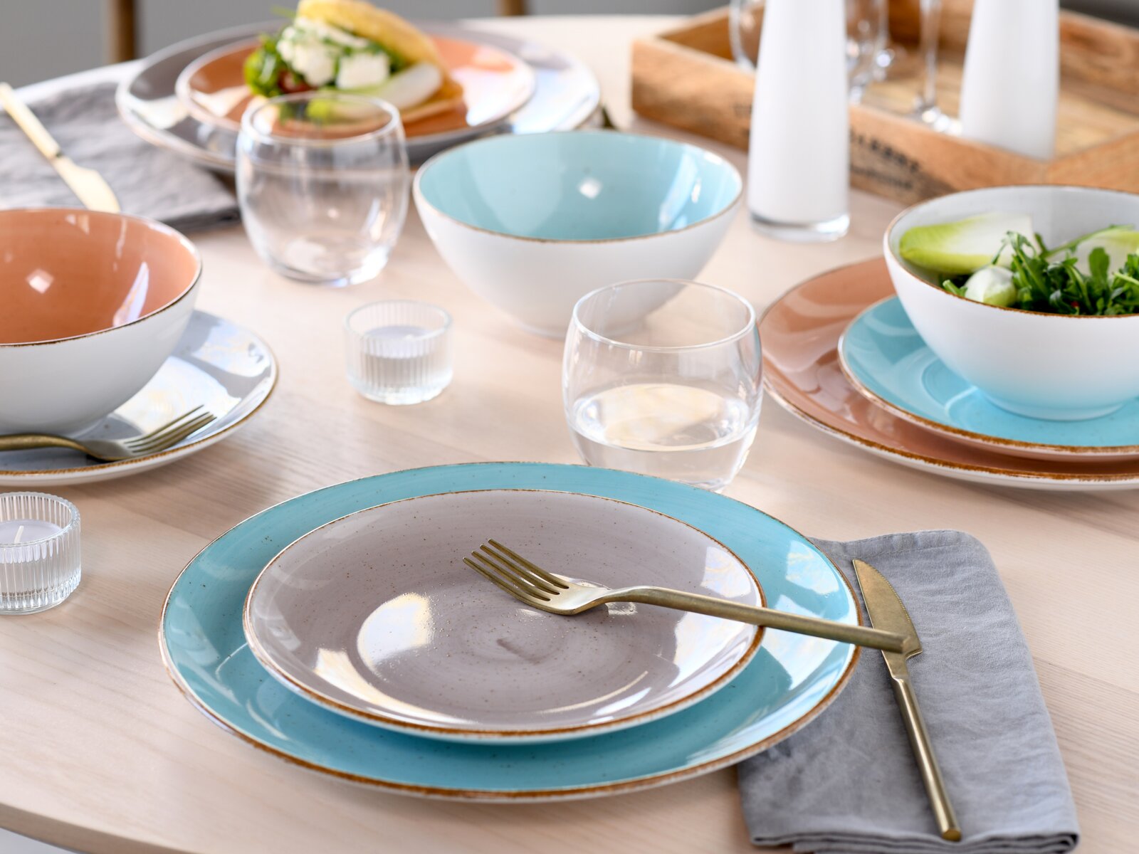 Creatable Kombiservice 16-tlg VINTAGE NATURE Schlicht gedeckter Esstisch mit Keramikgeschirr in Türkis, Grau und Terrakotta, Schalen und Tellern mit rustikalem Rand, Wassergläsern und goldenem Besteck, aufgenommen aus leicht erhöhter, schräger Perspektive von vorn.