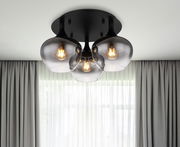 Moderne Deckenleuchte MAXY mit drei rauchgrauen Glaskugeln, von unten betrachtet, vor einem Fenster mit Vorhängen.