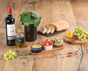 Akazienbrett mit drei Schalen, gefüllt mit Antipasti, auf einem Holztisch. Perspektive von oben.