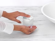 Seifenspender auf einer Marmoroberfläche, von oben betrachtet, mit einer Hand, die Seife aus dem Spender drückt.