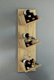 Wandmontiertes Weinregal aus hellem Holz mit drei schrägen Ablagen, jeweils mit mehreren Weinflaschen, frontal in leicht erhöhter Perspektive vor grauer Betonwand