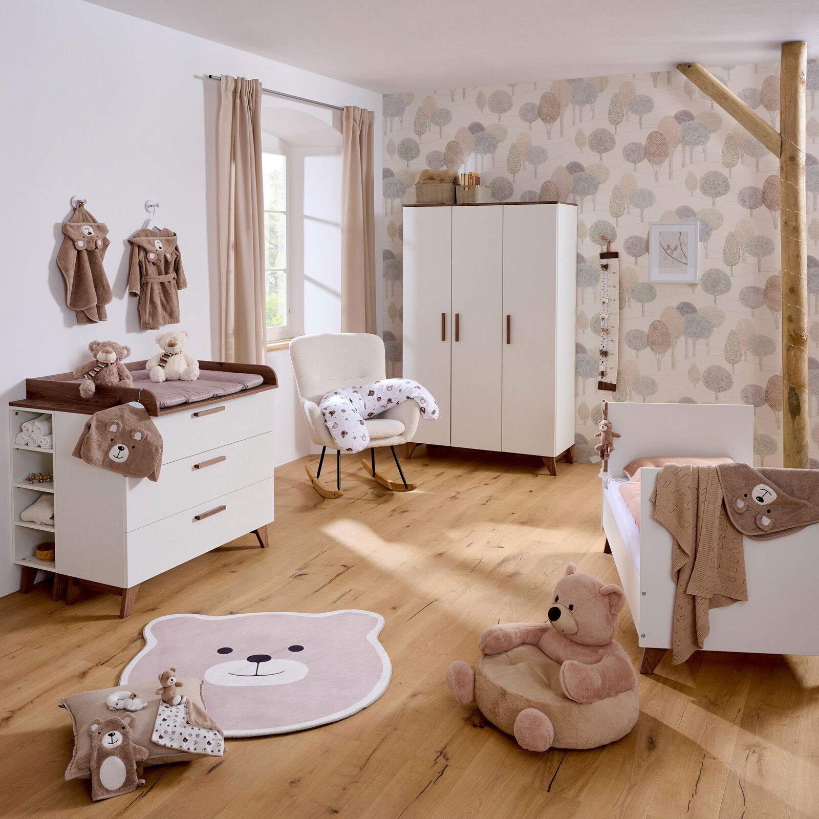 Kinderzimmer mit Babybett, Wickelkommode, Kleiderschrank und Bärendekoration, aus der Perspektive eines stehenden Betrachters.