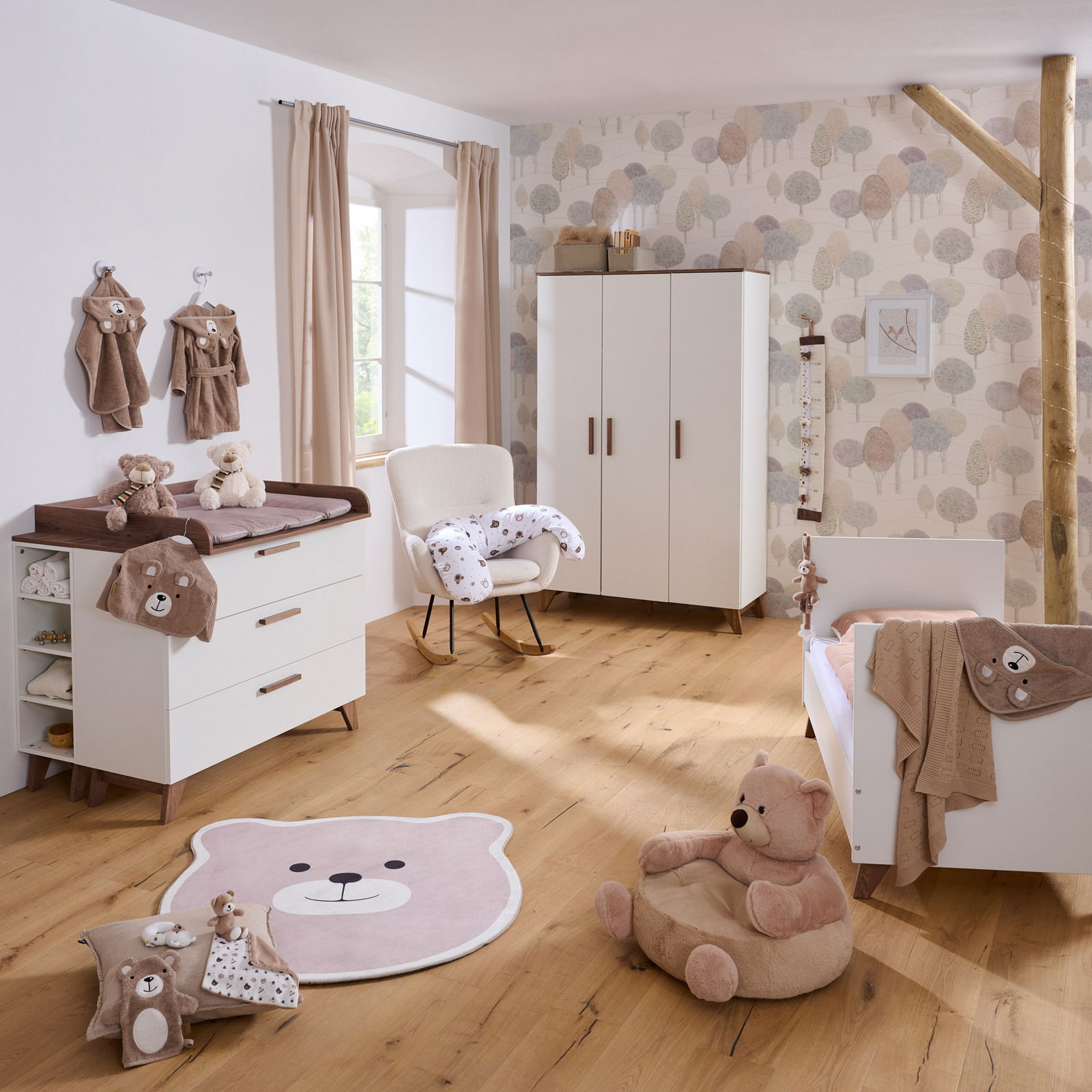 Kinderzimmer mit Babybett, Wickelkommode, Kleiderschrank und Bärendekoration, aus der Perspektive eines stehenden Betrachters.