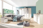 Modernes Schlafzimmer mit einem 180x200 cm großen Bett CAMRON, umgeben von stilvollen Möbeln in heller Holzoptik. Perspektive: seitliche Ansicht des Bettes mit Blick auf den Raum.