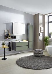 Moderne Badkombination in einem stilvollen Badezimmer, bestehend aus einem Waschtisch mit Unterschrank, einem hohen Schrank und einem beleuchteten Spiegelschrank, aus seitlicher Perspektive fotografiert.