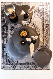 Vogelperspektive auf einen stilvollen Beistelltisch mit mehreren runden Ebenen, dekoriert mit einer Lampe, Vasen und Nüssen auf einem gemusterten Teppich.