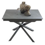 Moderner Esstisch TOKYO mit grauer Tischplatte und stilvollem, gekreuztem Metallgestell, dekoriert mit Vasen und Skulptur, aus seitlicher Perspektive.