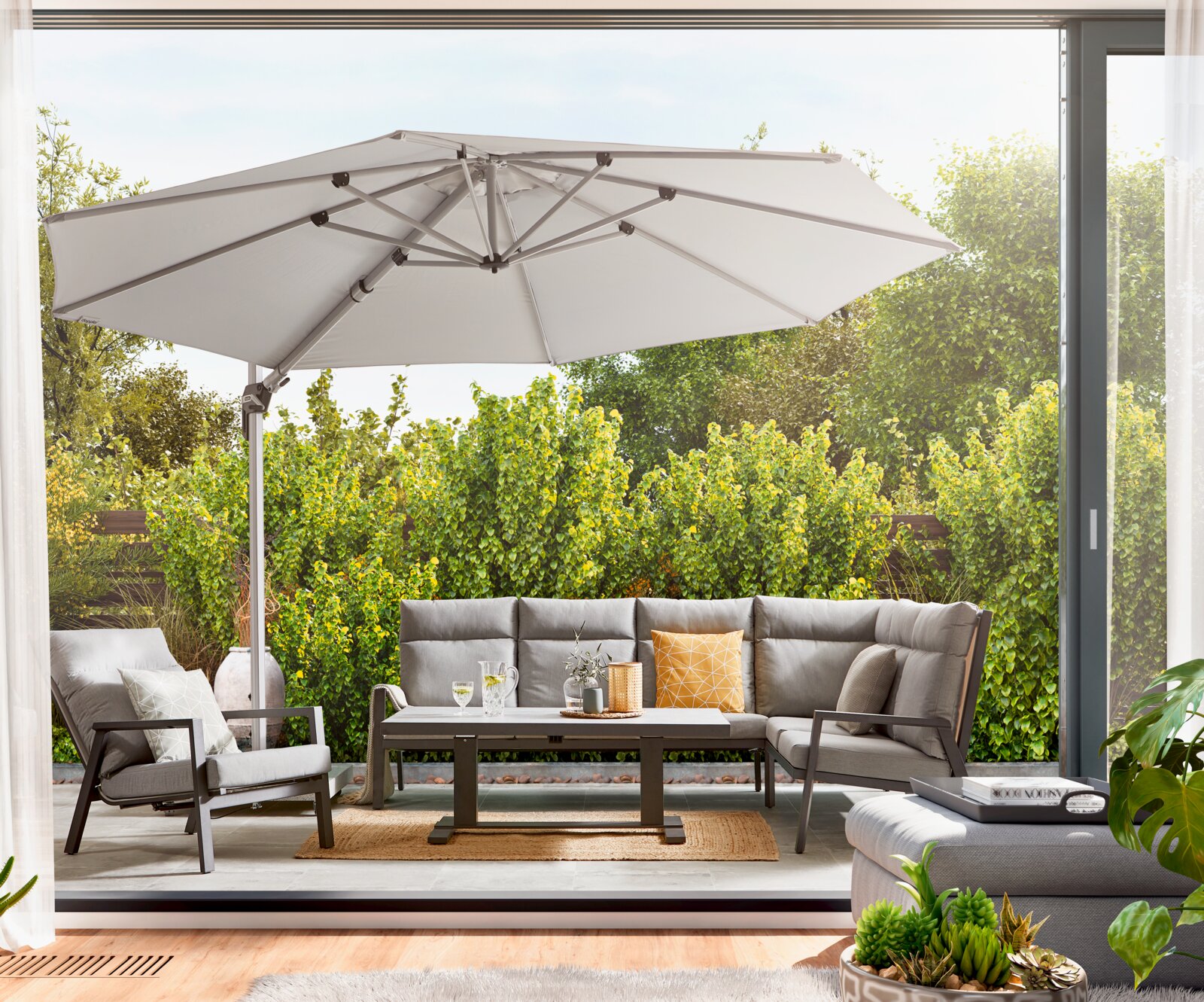 Amatio Pro Tuintafel LUZERN Een moderne tuintafel op een terras, omringd door comfortabele stoelen en een grote parasol, gezien vanuit een open woonkamer met uitzicht op de tuin.