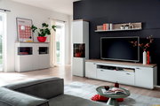 Modernes Wohnzimmer-Set mit weißer TV-Bank, Vitrine und Sideboard mit Holzoptik-Abdeckplatten vor dunkler Akzentwand, frontal in leichter Weitwinkelperspektive aufgenommen