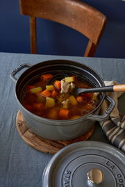 Runder Bräter Cocotte 24cm in Grau, gefüllt mit Eintopf, auf einem Tisch von oben fotografiert.