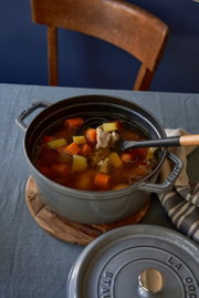 Runder Bräter Cocotte 24cm in Grau, gefüllt mit Eintopf, auf einem Tisch von oben fotografiert.