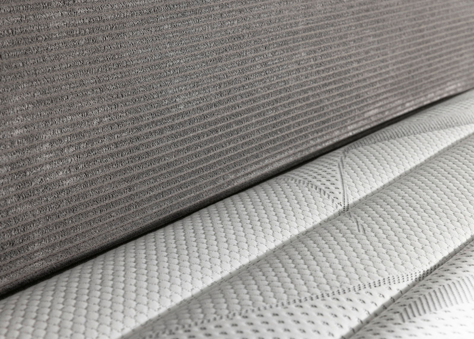 Nahaufnahme eines Boxspringbetts 180x200 mit grauem Stoffbezug und weißer, strukturierter Matratze, seitliche Perspektive