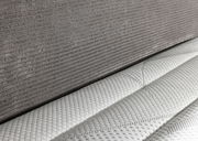 Nahaufnahme eines Boxspringbetts 180x200 mit grauem Stoffbezug und weißer, strukturierter Matratze, seitliche Perspektive