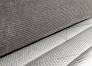 Nahaufnahme eines Boxspringbetts 180x200 mit grauem Stoffbezug und weißer, strukturierter Matratze, seitliche Perspektive