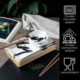 Sushi Set aus Porzellan mit schwarzer Schrift, bestehend aus rechteckigen Tellern und runden Schalen, präsentiert auf einem Tisch mit Essstäbchen und einem Buch im Hintergrund, aus der Vogelperspektive.