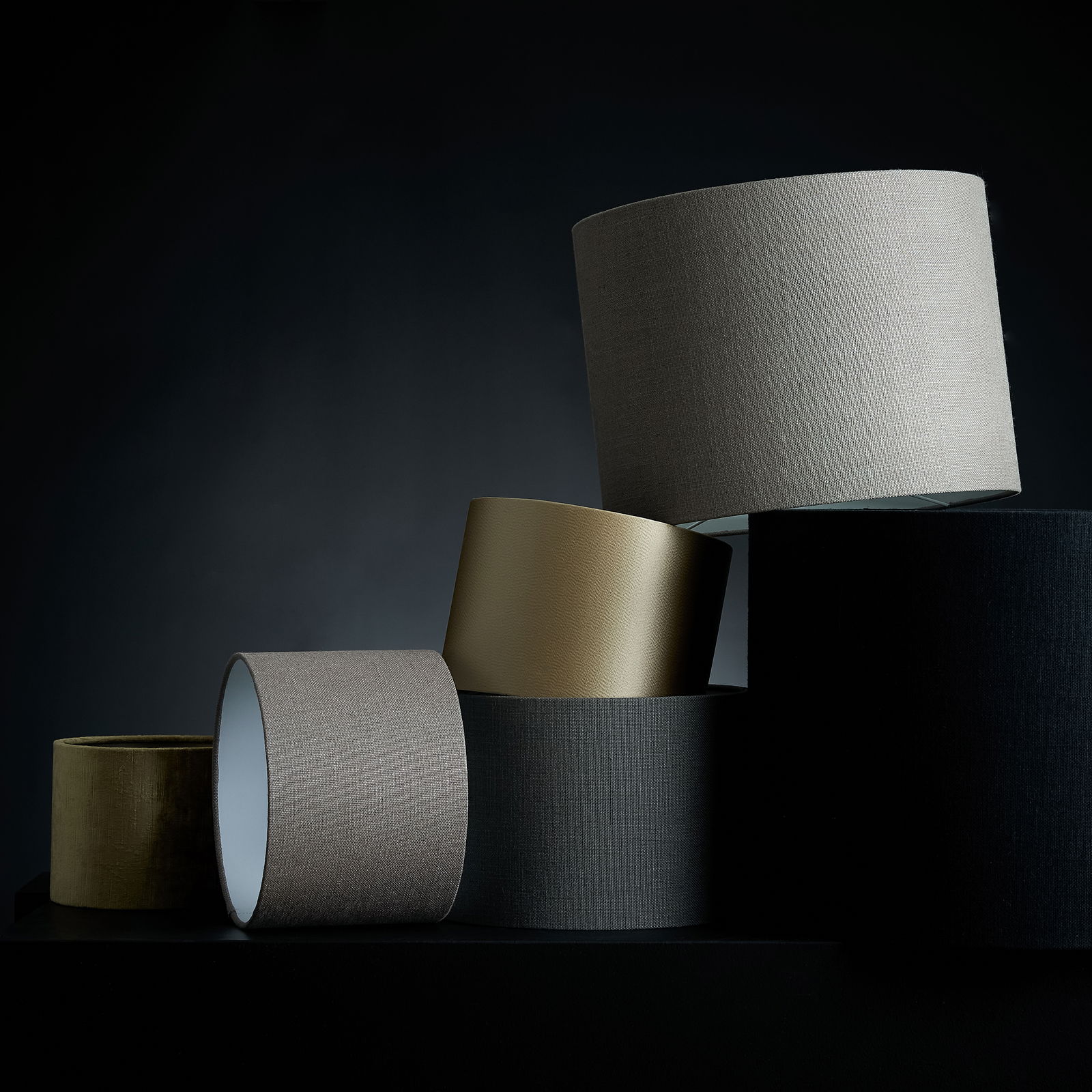 Mehrere Lampenschirme in verschiedenen Farben und Texturen, gestapelt in einer künstlerischen Anordnung, seitliche Perspektive