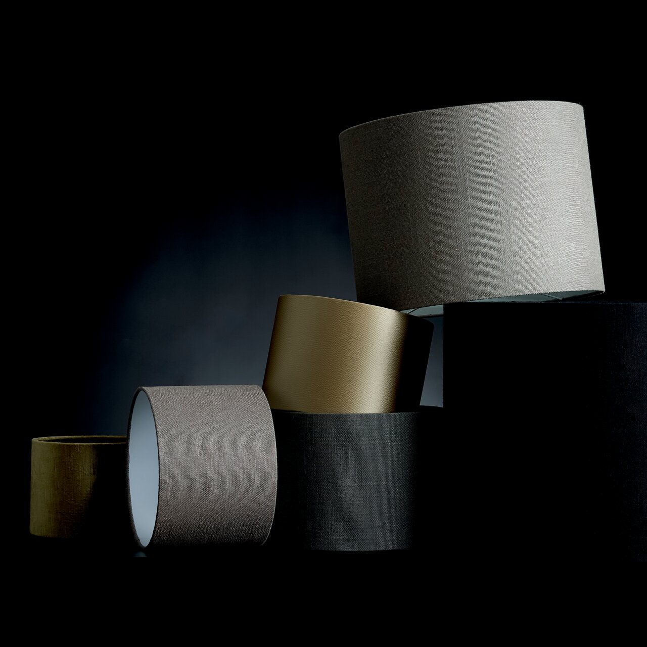 Mehrere Lampenschirme in verschiedenen Farben und Texturen, gestapelt in einer künstlerischen Anordnung, seitliche Perspektive