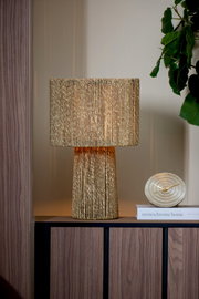 Goldene Tischuhr BOJANO mit einem Durchmesser von 15,5 cm, frontal auf einem Regal neben einer dekorativen Lampe und einem Buch platziert.